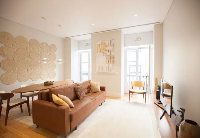 A bright living room features a sofa, dining table, and large windows.