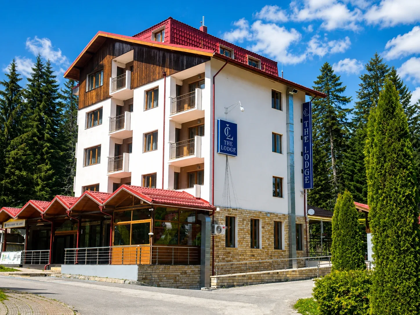 Espacio representativo del hotel: Un hotel de varios pisos con balcones y techo rojo está rodeado de árboles.