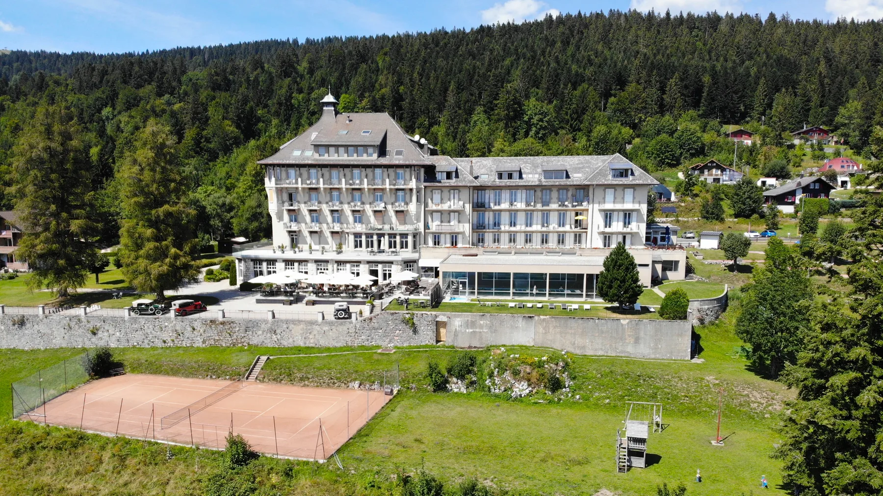 Representative hotel space: A large hotel stands beside a fenced tennis court, with forested hills behind it.