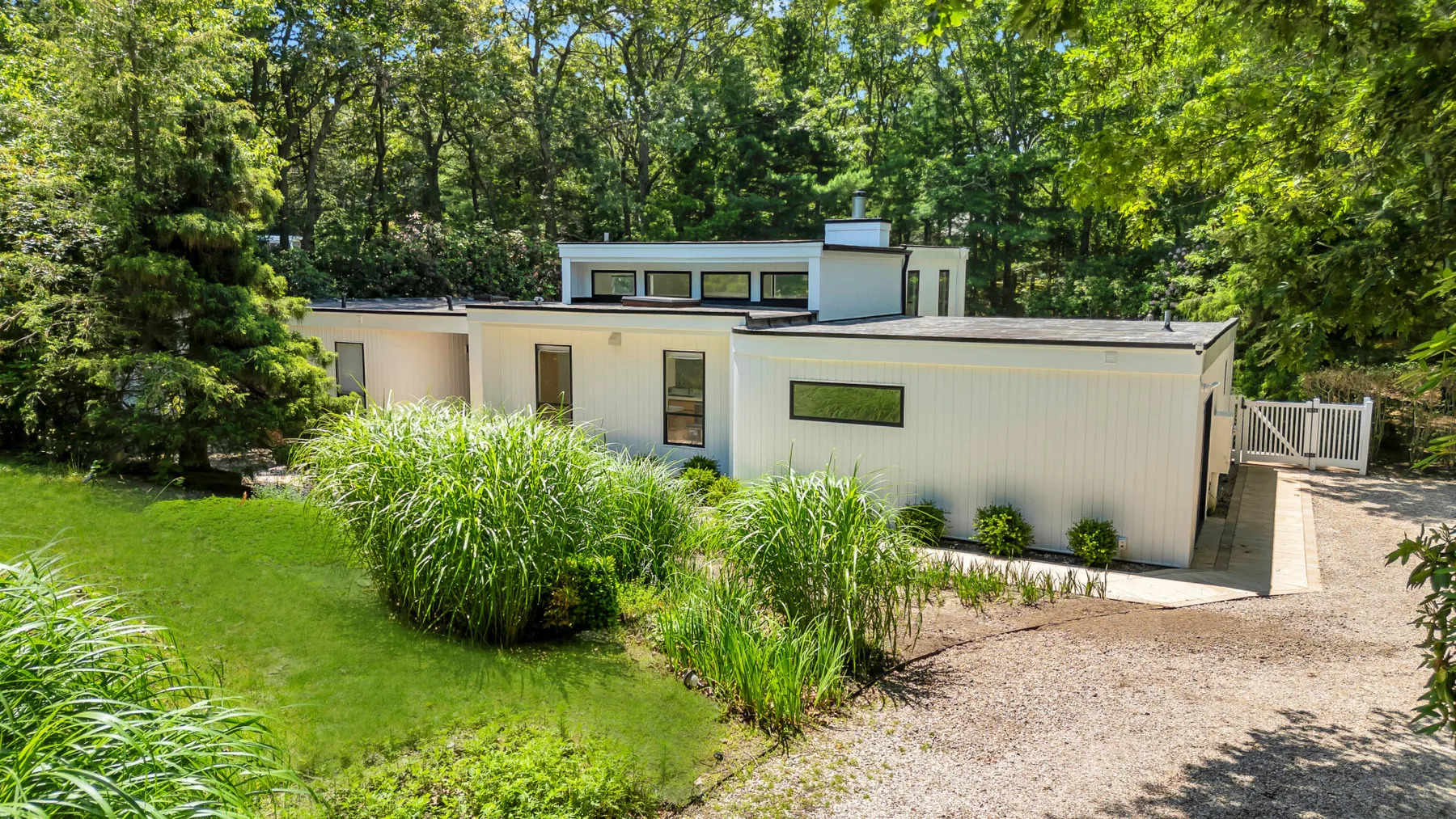 A modern low-rise building sits beside a gravel path, surrounded by trees and greenery.