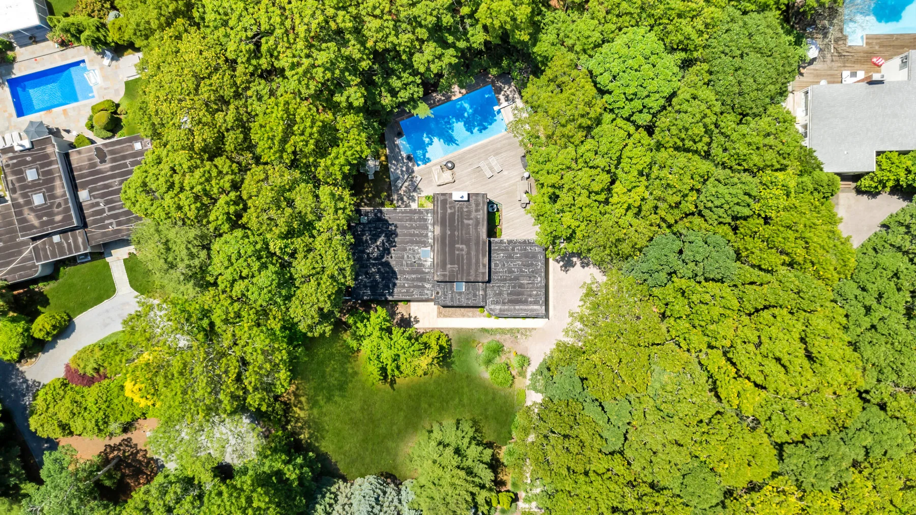 An aerial view of a tree-lined property with a house, lawn, and swimming pool.