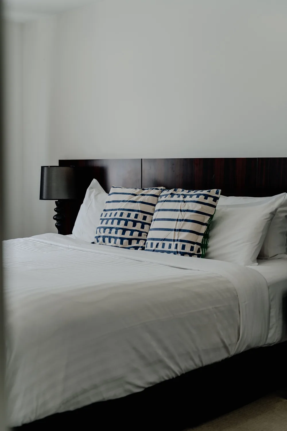 A neatly made bed with patterned pillows against a dark headboard.