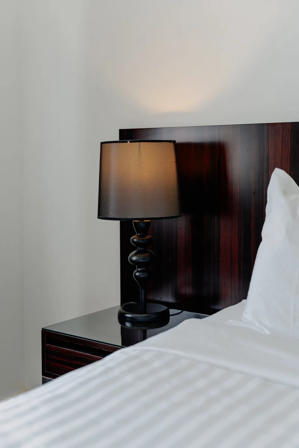 A bedroom with a bedside lamp beside a neatly made bed.