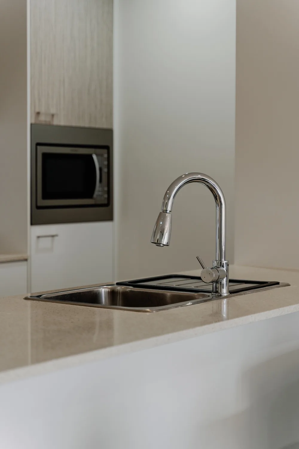 A kitchen sink and curved faucet are set into a light countertop.