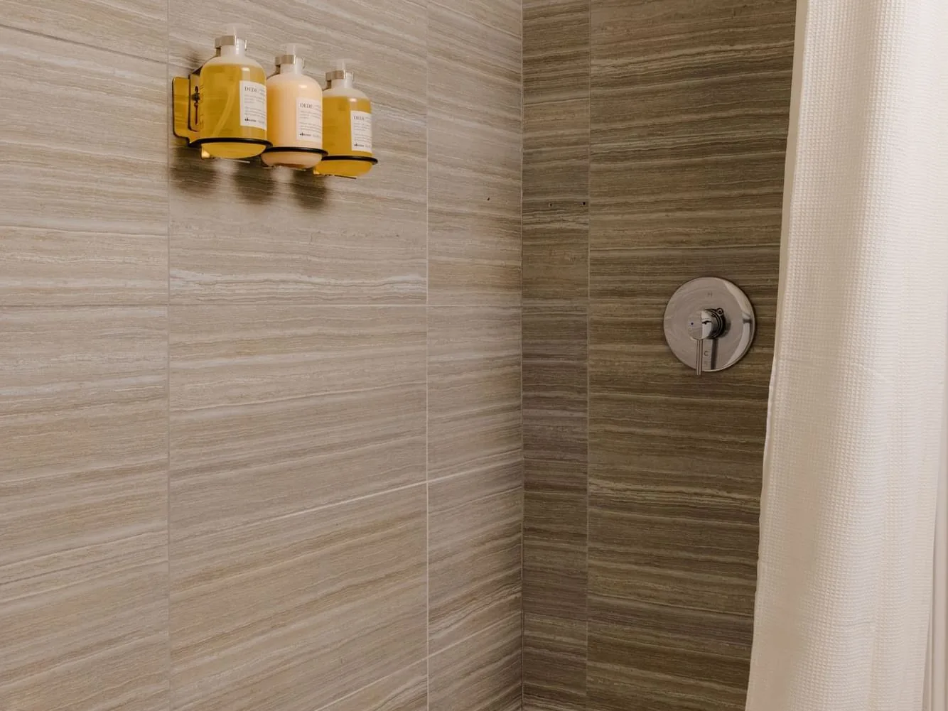 Espacio representativo del hotel: Una zona de ducha con azulejos, botellas en la pared y un control de ducha.