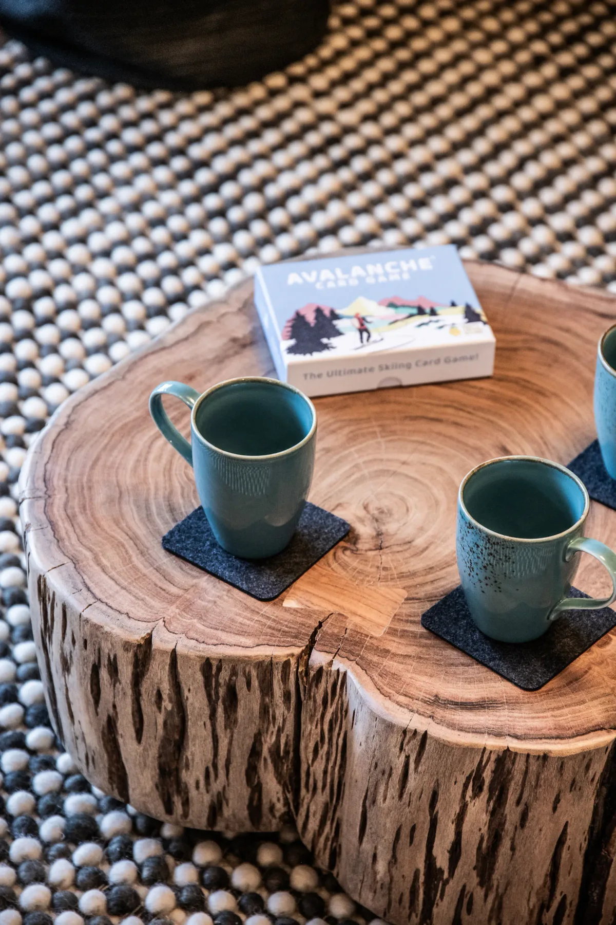 Two mugs and a board game sit on a low wooden table over a pebble-patterned rug.