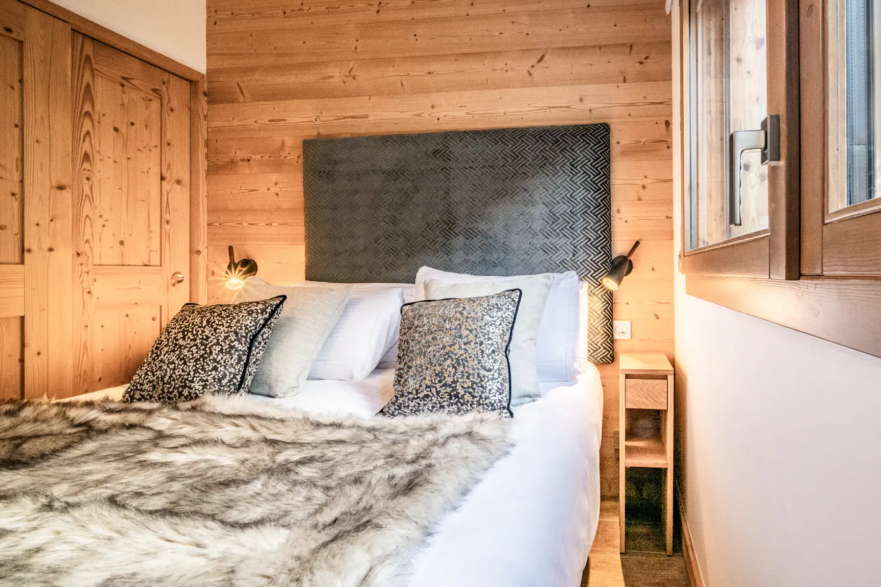 A bedroom with a bed covered in a patterned throw beneath a dark headboard.