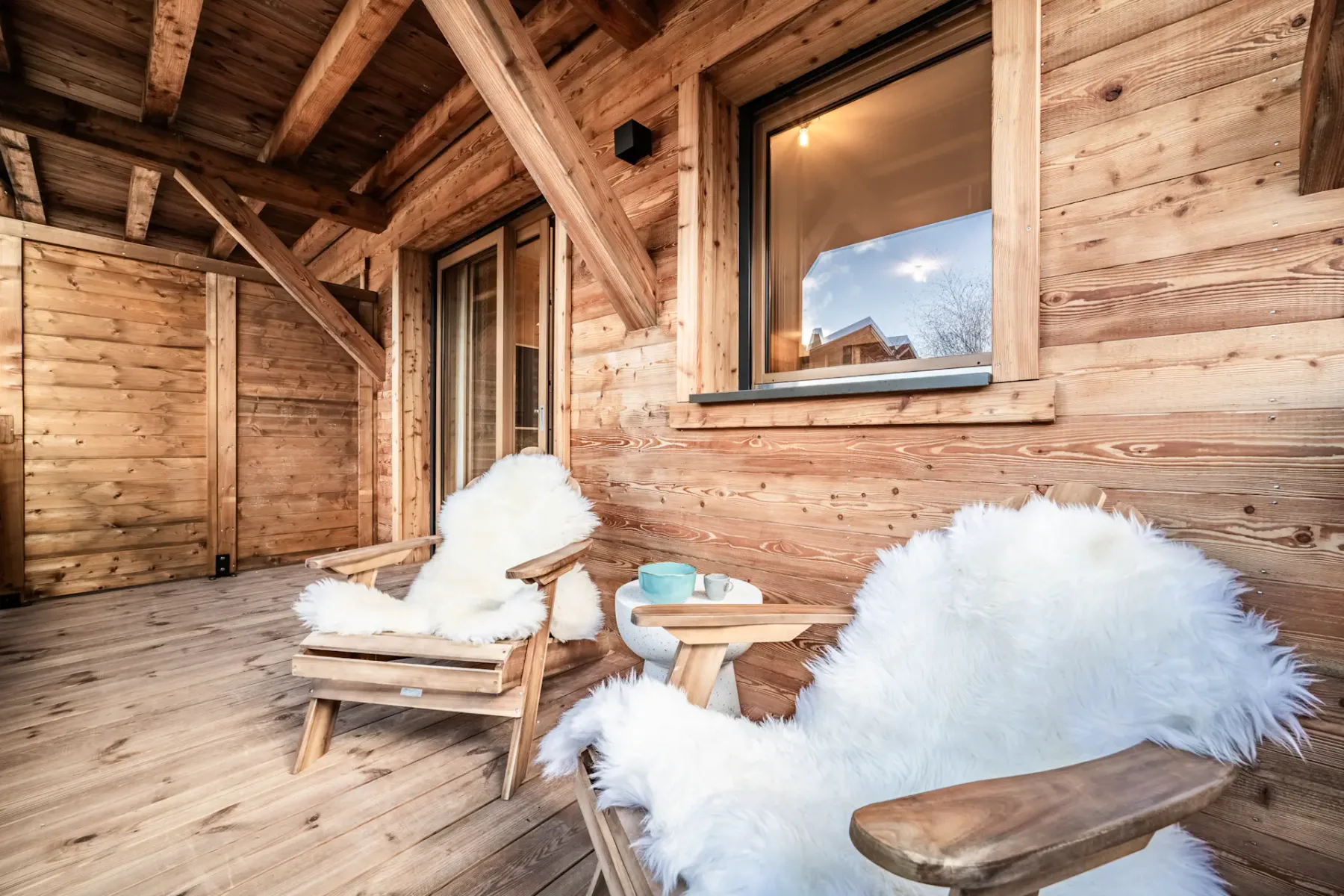 A rustic wooden porch with seating and fluffy white covers.