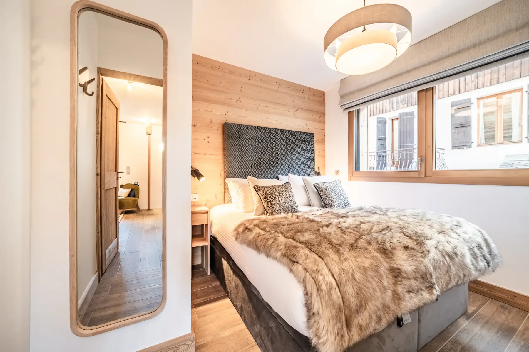 A bedroom with a bed dressed in layered bedding beside a wood-paneled wall.