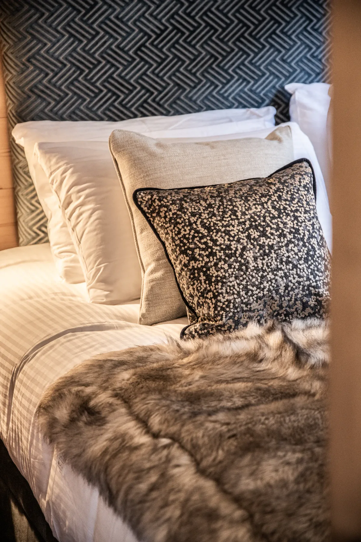 A neatly made bed with layered pillows and a patterned dark headboard.