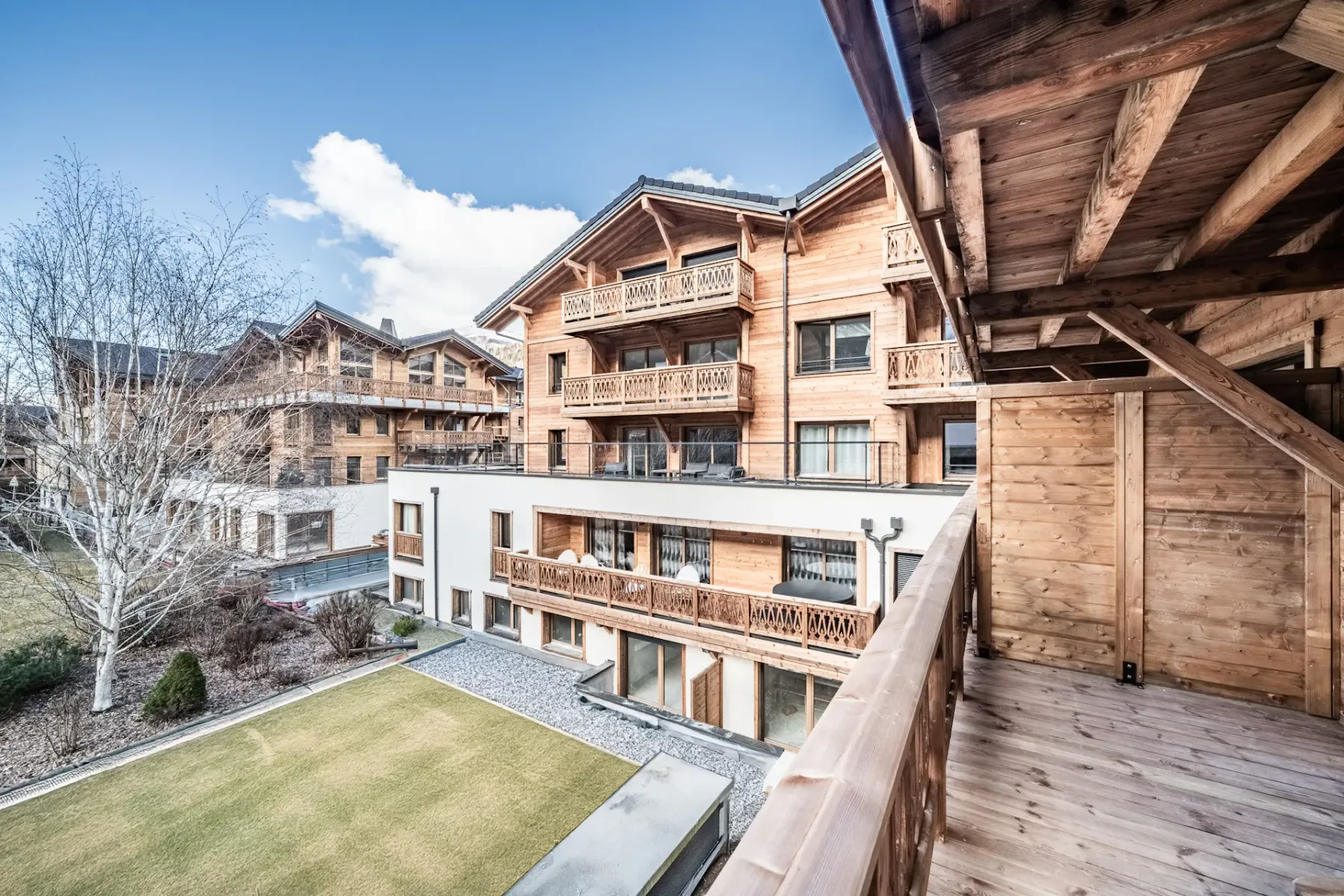 A wooden balcony overlooks timber-clad buildings and a landscaped courtyard.
