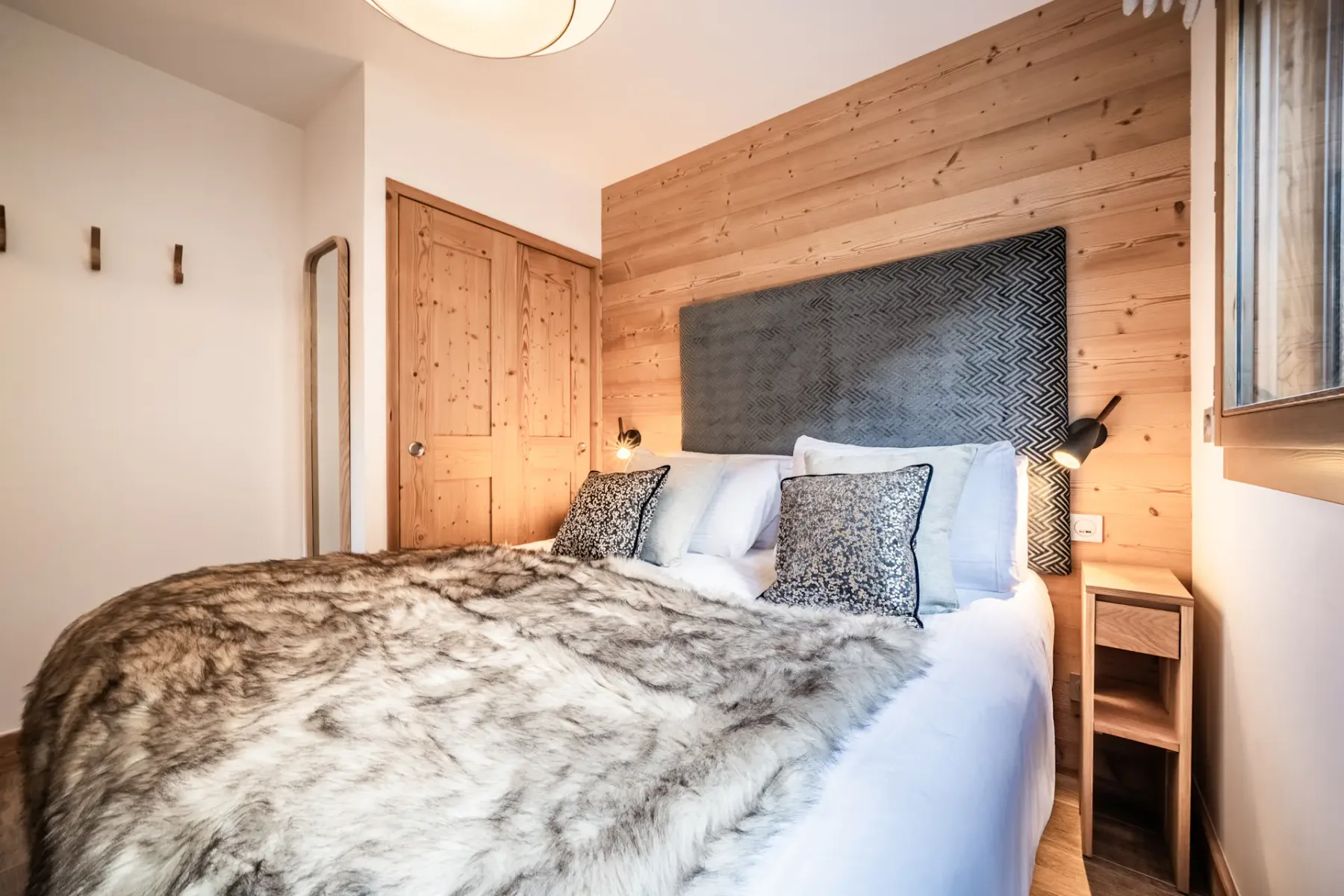A bedroom with a bed covered by a patterned blanket and wood-paneled walls.