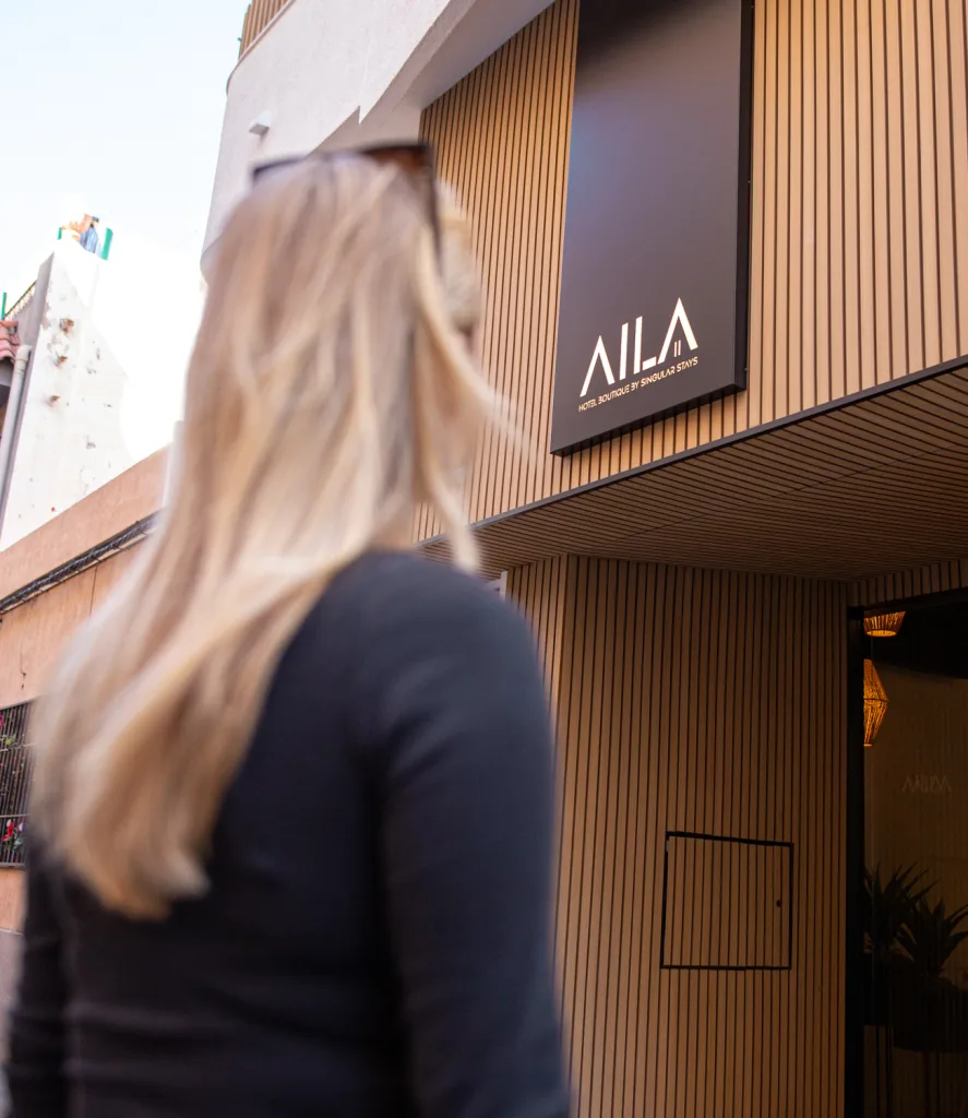 Espacio representativo del hotel: Una mujer mira la entrada de un edificio moderno con una fachada de listones verticales.