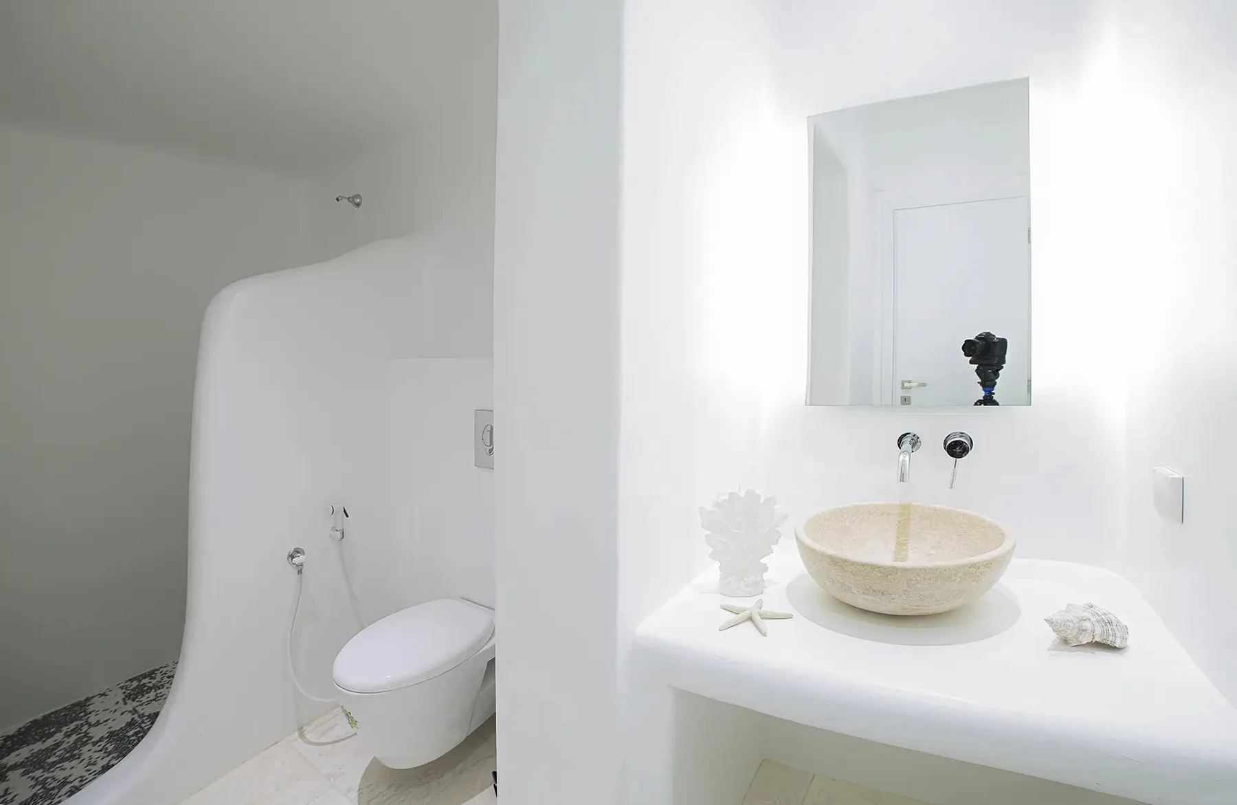 A bright white bathroom with a toilet and a vessel sink on the counter.