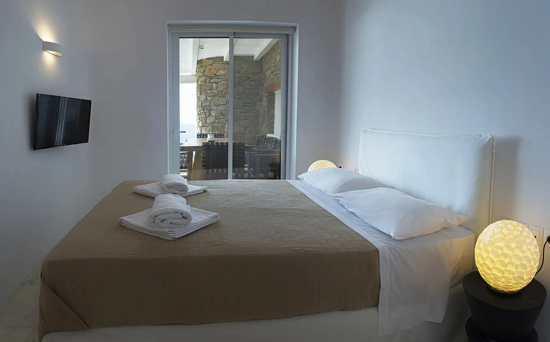A bedroom with a neatly made bed and a glass door opening onto a stone patio.
