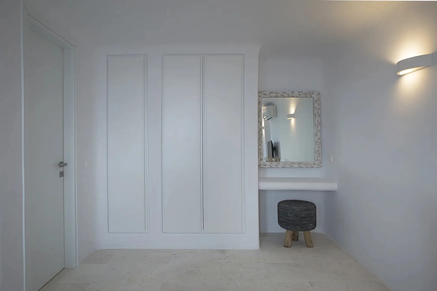 A bright dressing area with built-in cabinets, a mirror, and a small seat.