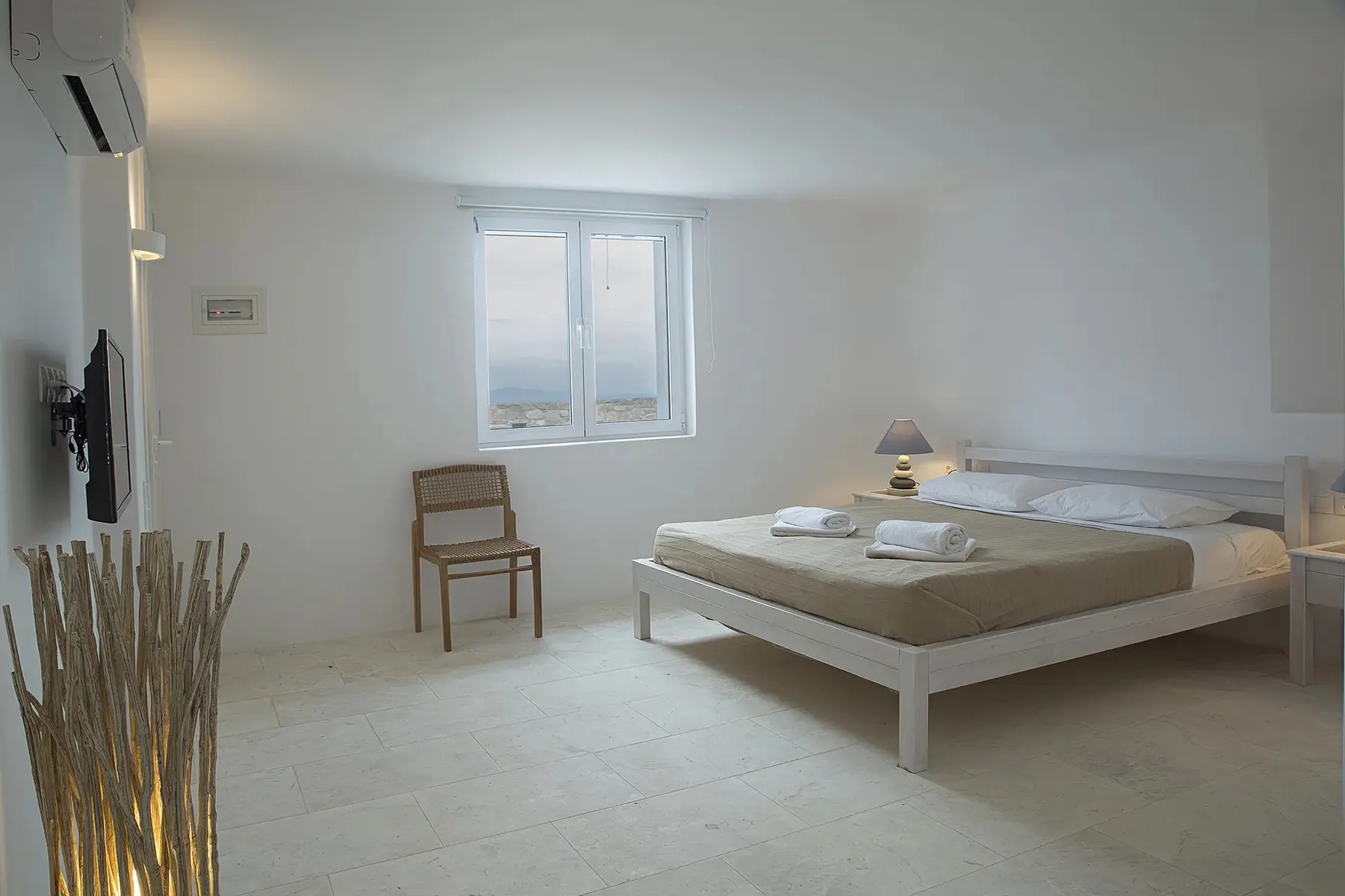 A bright bedroom with a double bed, a window, and a small bedside lamp.