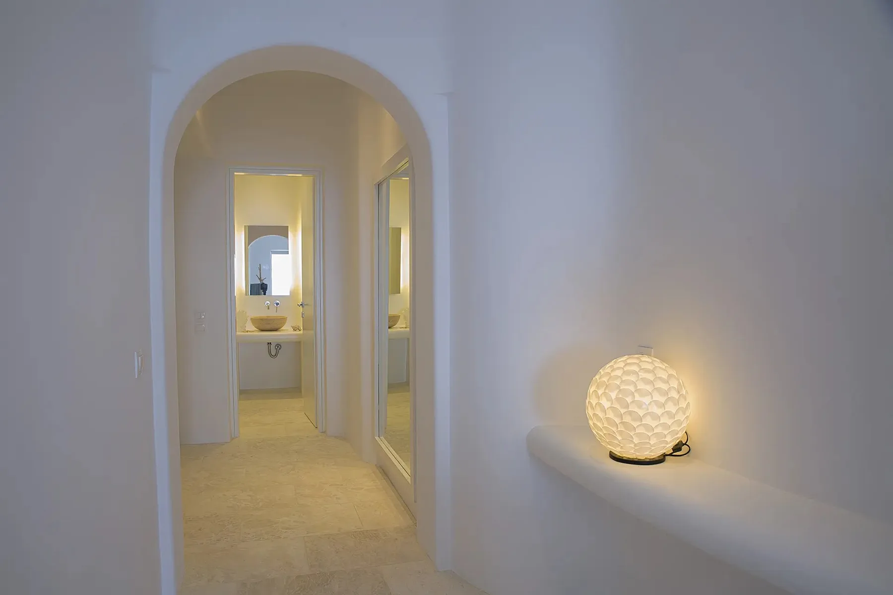 A softly lit hallway with an arched doorway and a glowing lamp on a ledge.