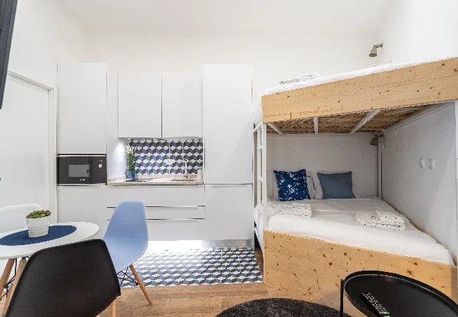 Un dormitorio compacto con una cama elevada y una pequeña cocina.