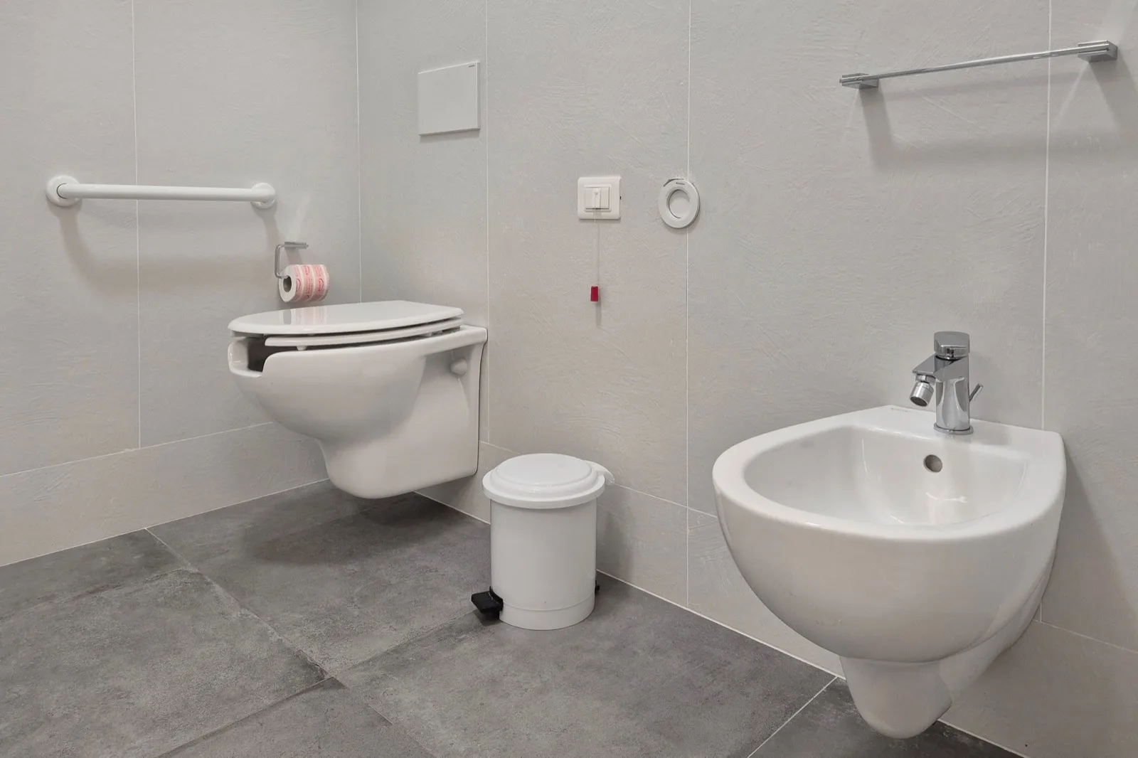 Representative hotel space: A tiled bathroom with a wall-mounted toilet and a sink.