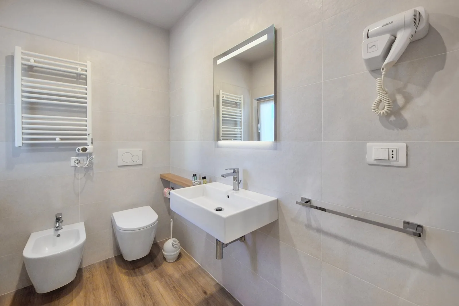 Representative hotel space: A tiled bathroom with a sink, toilet, and wall-mounted hair dryer.