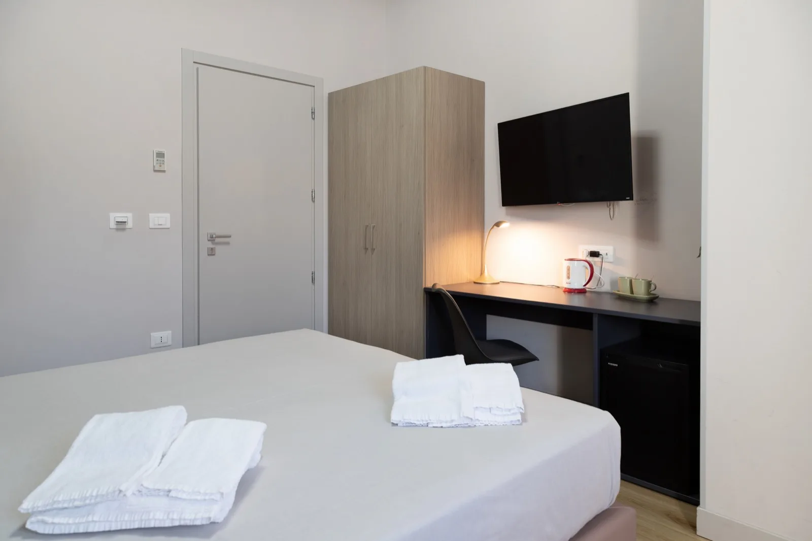 Representative hotel space: A guest bedroom with a bed, wardrobe, and desk beneath a wall-mounted television.