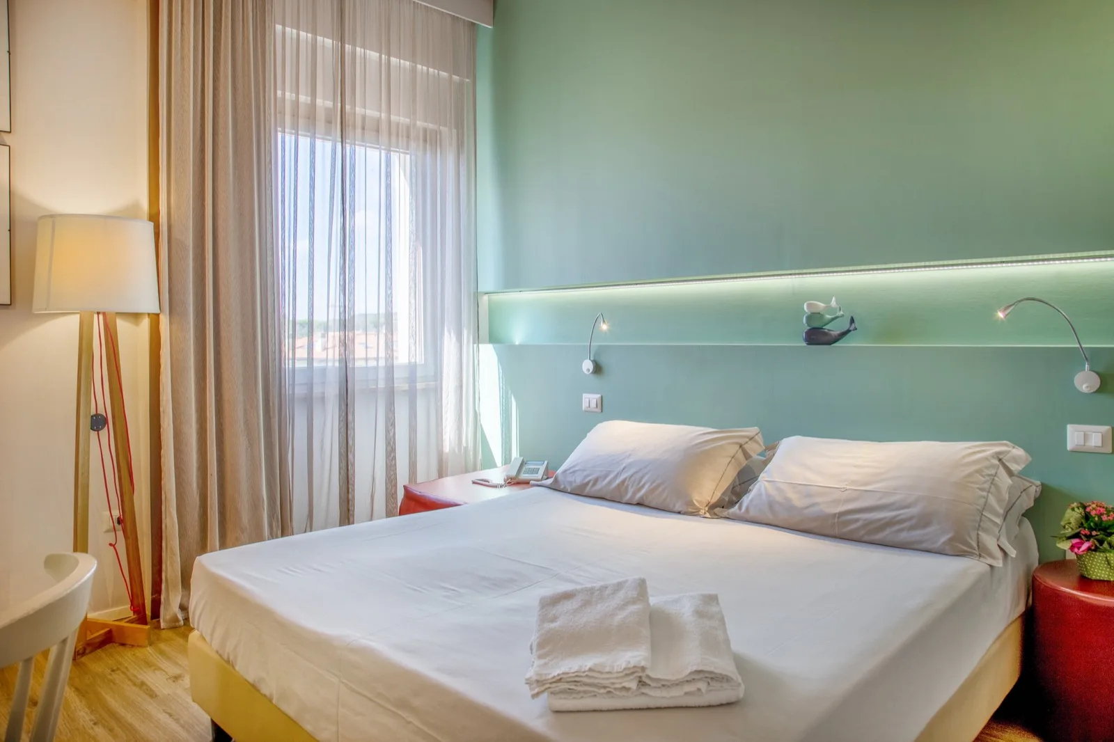 Representative hotel space: A bedroom with a neatly made bed and a large curtained window.