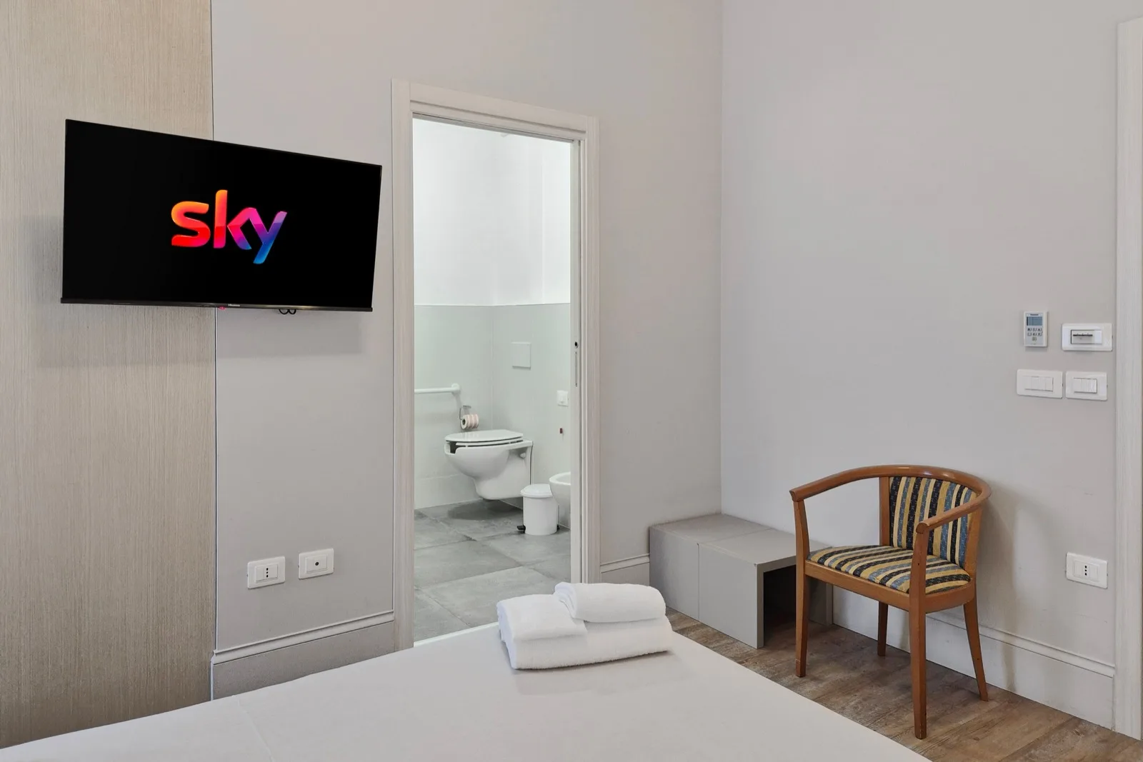 Representative hotel space: A bedroom with a wall-mounted television, seating, and an open bathroom doorway.