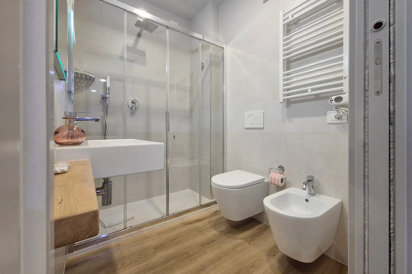 Representative hotel space: A modern bathroom with a glass shower, wall-mounted sink, toilet, and bidet.