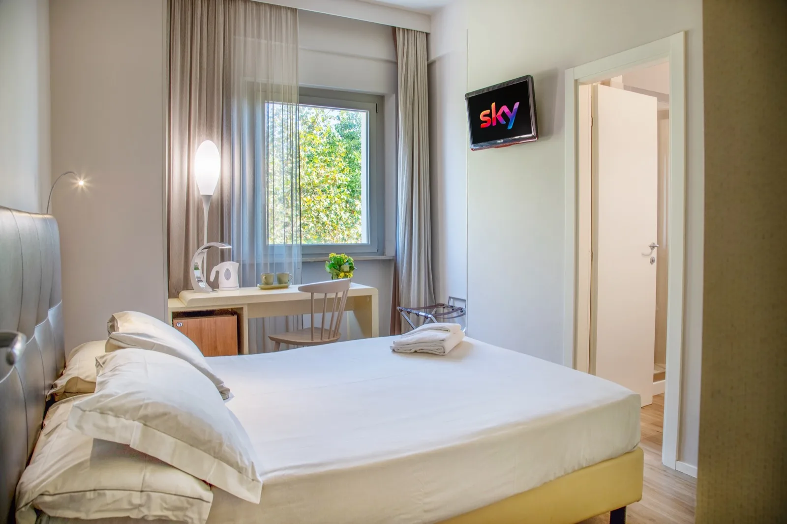 Representative hotel space: A bedroom with a neatly made bed, a window, and a small desk.