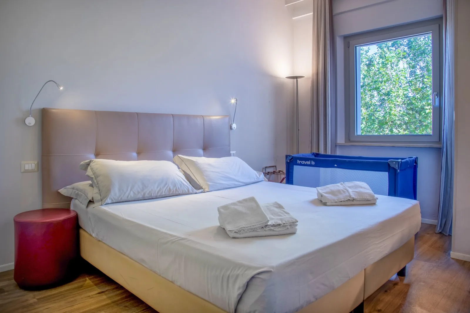 Representative hotel space: A bedroom with a large bed and a window overlooking leafy trees.