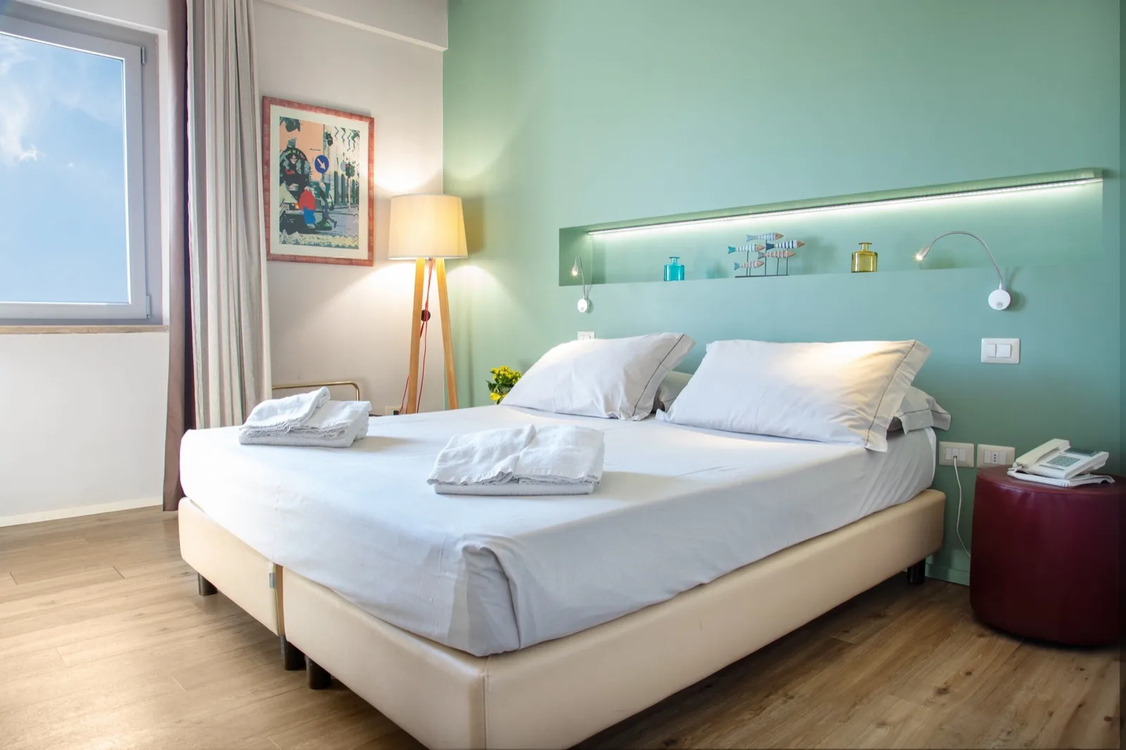 Representative hotel space: A bright bedroom with a neatly made bed beneath a teal wall.