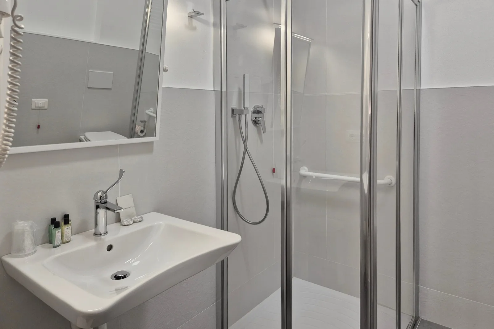 Representative hotel space: A bathroom with a sink, mirror, and glass-enclosed shower.