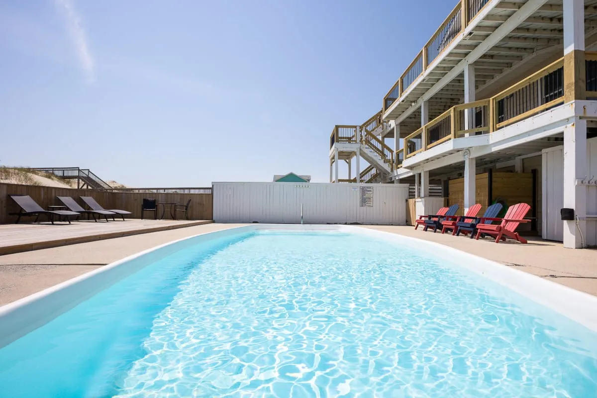 An outdoor swimming pool beside a raised building with seating along the deck.