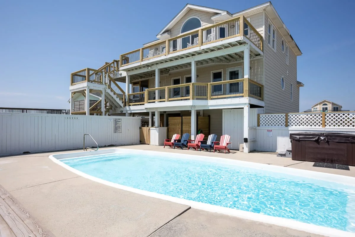 A coastal-style house overlooks a swimming pool, with outdoor seating beside it.