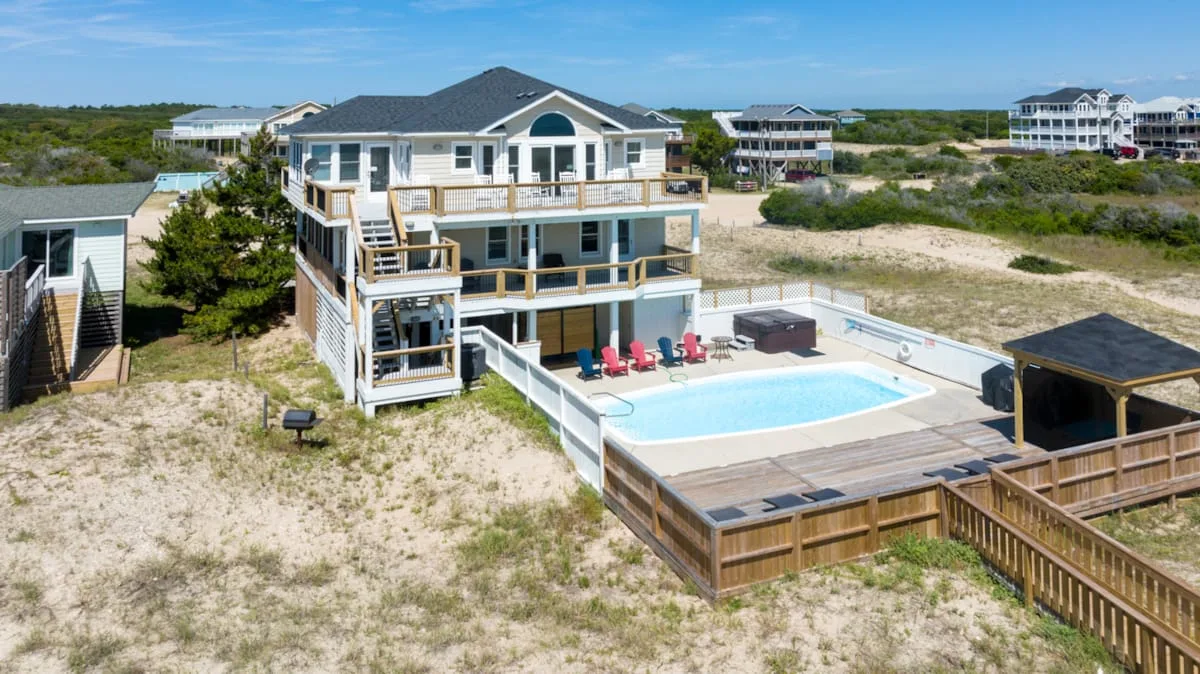 A large coastal house stands beside a fenced swimming pool.