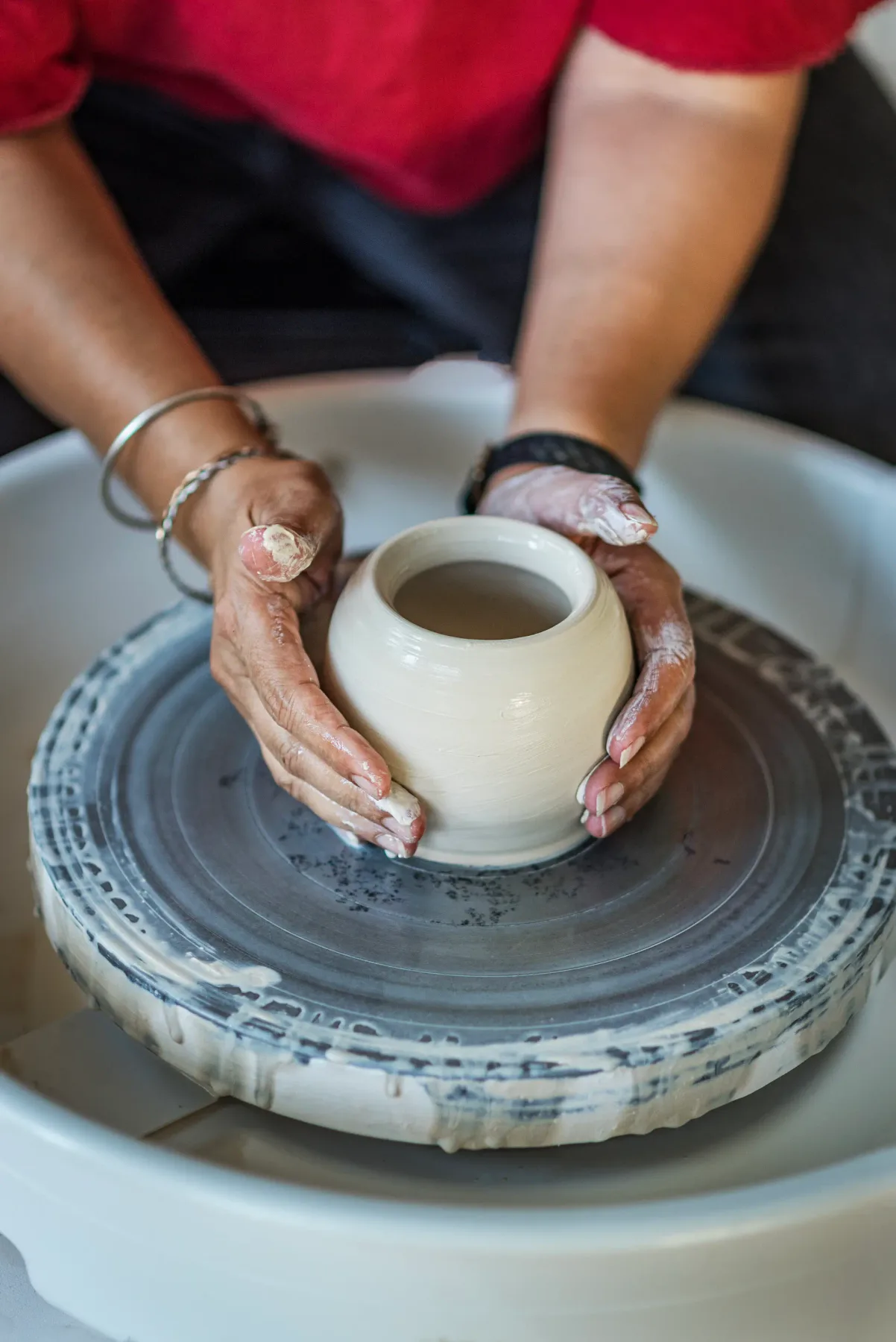 A person shapes a clay vessel on a pottery wheel.