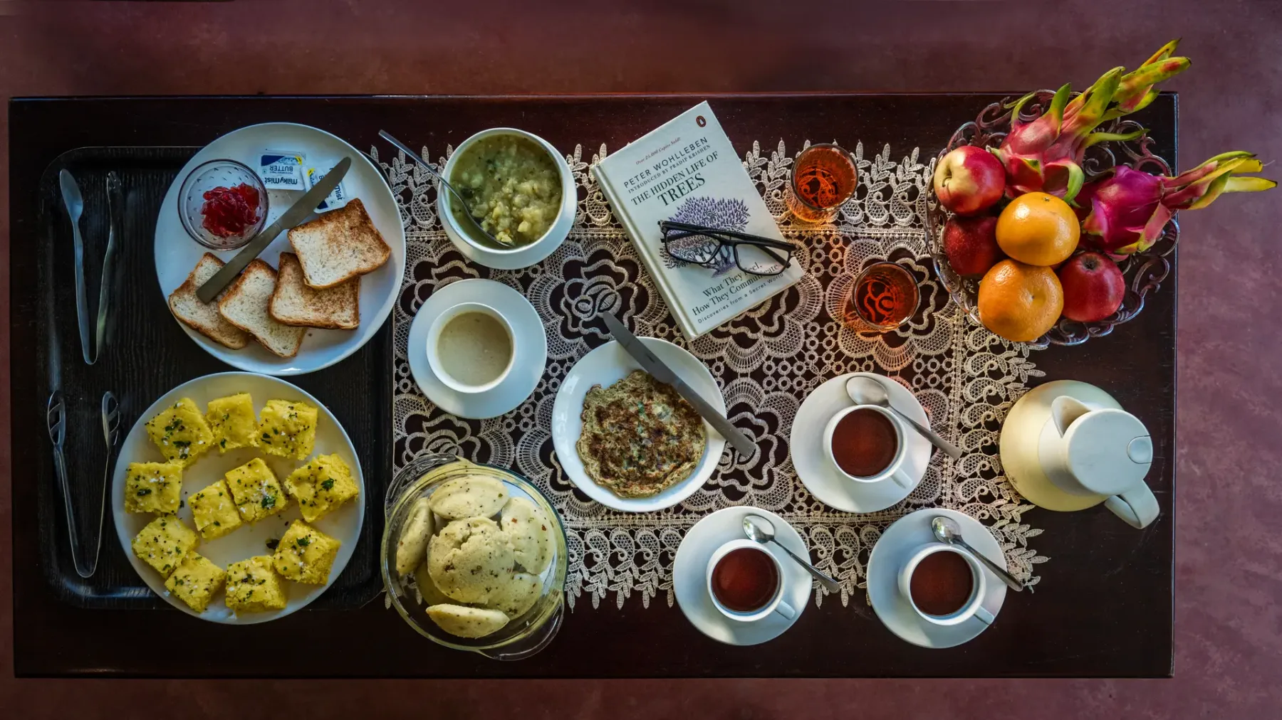 A breakfast spread on a table includes toast, fruit, cups, and small dishes.