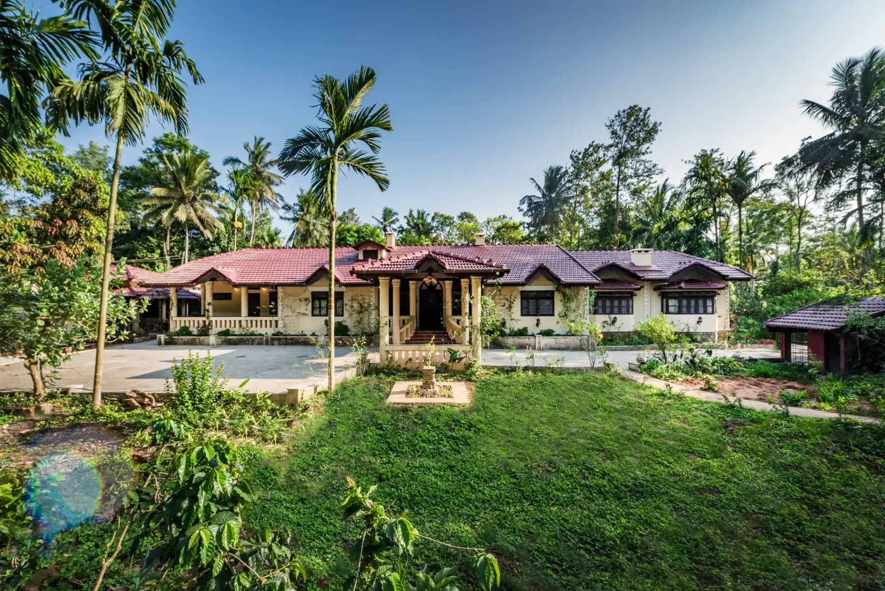 A single-story house with a red tiled roof sits among palms and greenery.