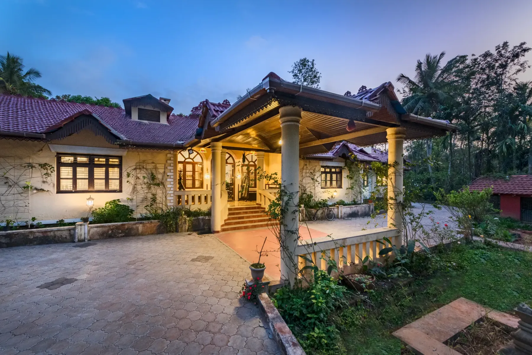 A warmly lit house entrance with a covered porch and paved courtyard.
