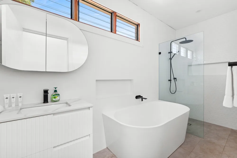 Un baño luminoso cuenta con una bañera exenta y una mampara de ducha de vidrio.