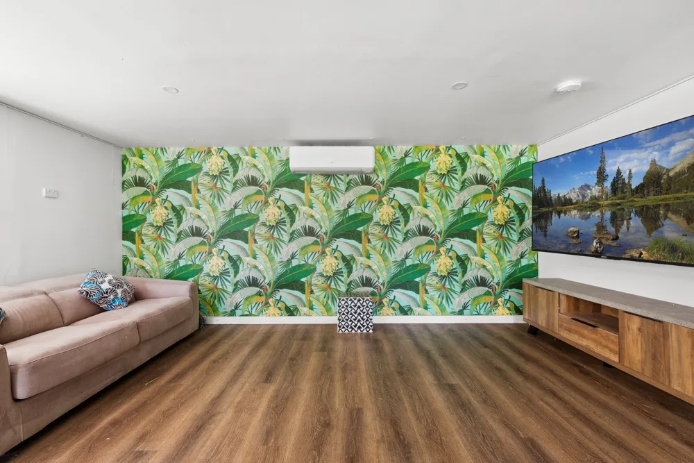 Una sala de estar con papel tapiz de hojas tropicales, asientos y un mueble de madera.