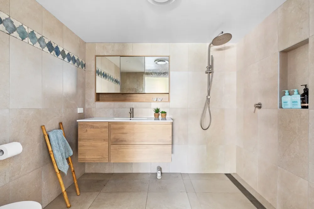 Un baño alicatado con tocador de madera, espejo y ducha de pared.