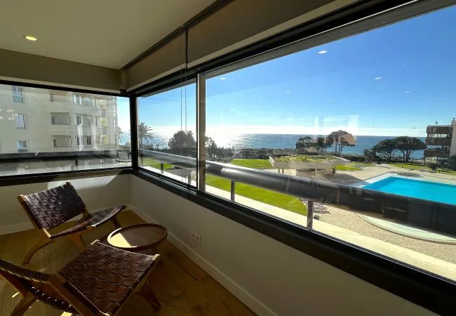 A sunlit enclosed seating area overlooks a pool and the ocean.