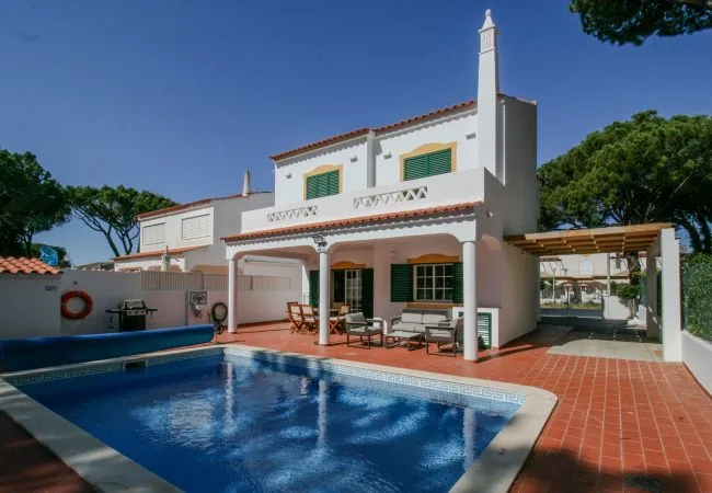 Una casa blanca de dos plantas da a una piscina y un patio de terracota.