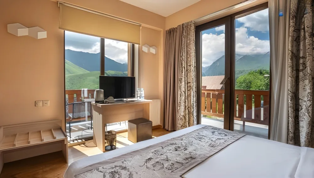 Representative hotel space: A bedroom with a desk beside large windows overlooking green mountains.