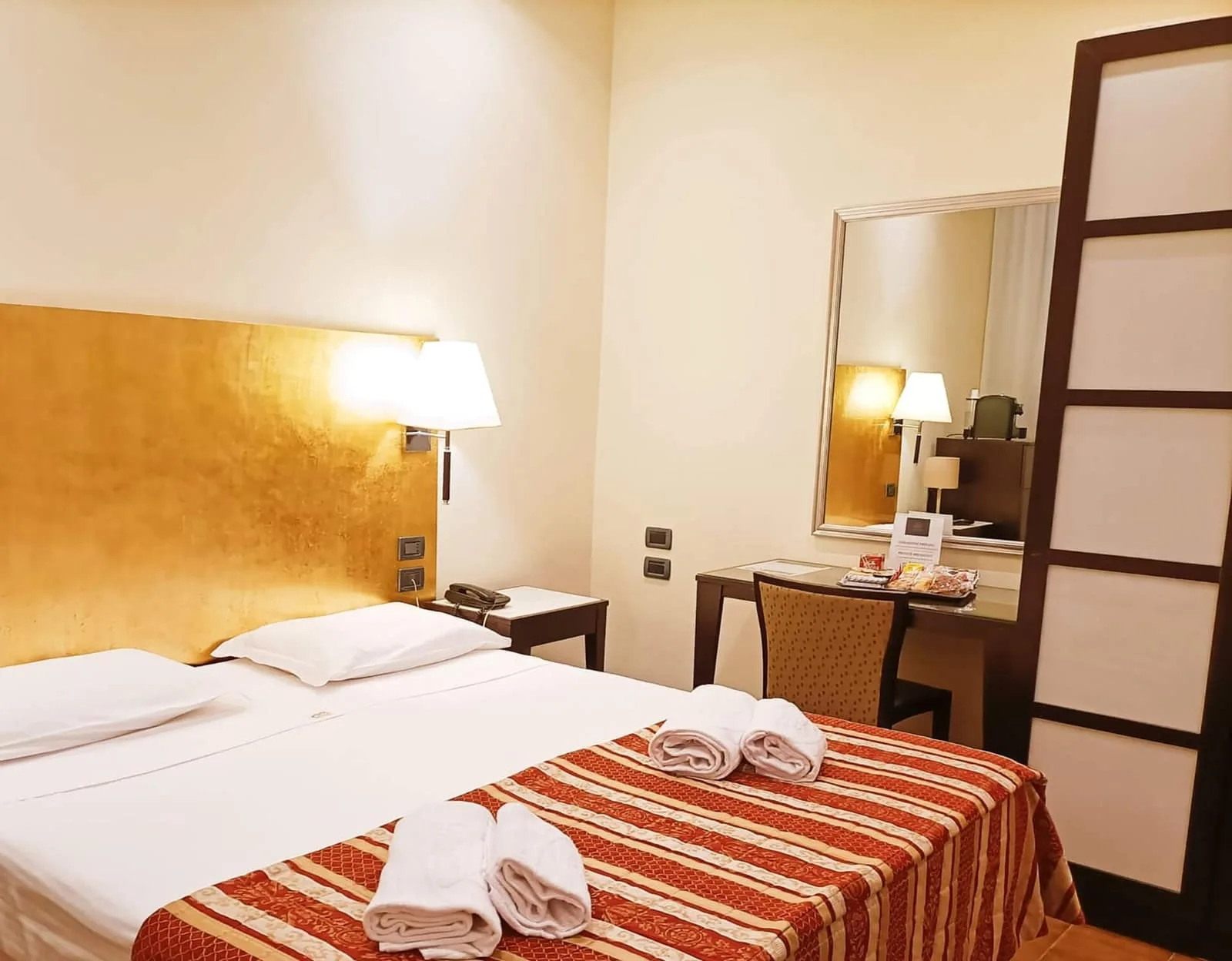 Representative hotel space: A hotel bedroom with a bed, bedside lamp, and desk.