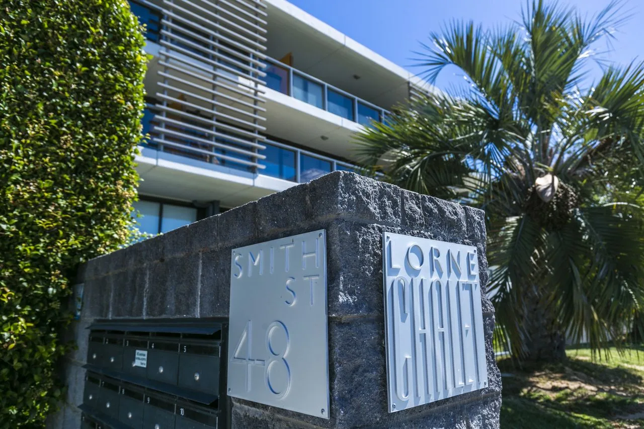 Zona común: Un edificio residencial aparece detrás de un letrero de piedra y buzones.