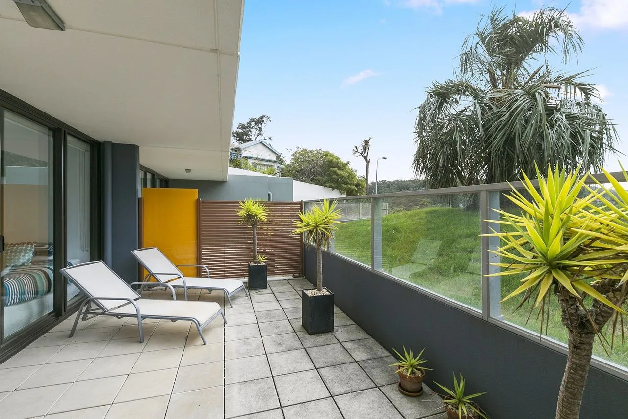Un patio exterior embaldosado con asientos, plantas en macetas y una barandilla de vidrio.