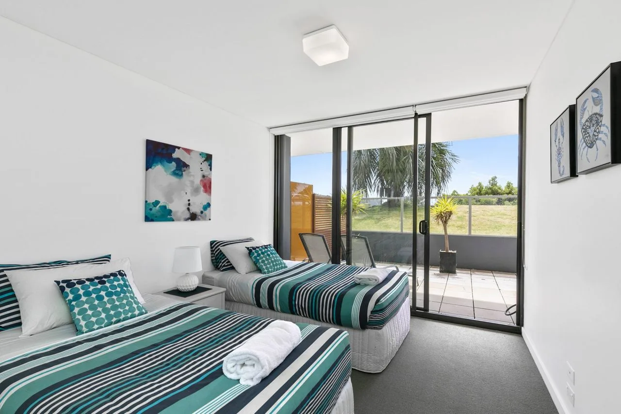 Un dormitorio luminoso con dos camas y puertas corredizas de vidrio que dan a un patio.